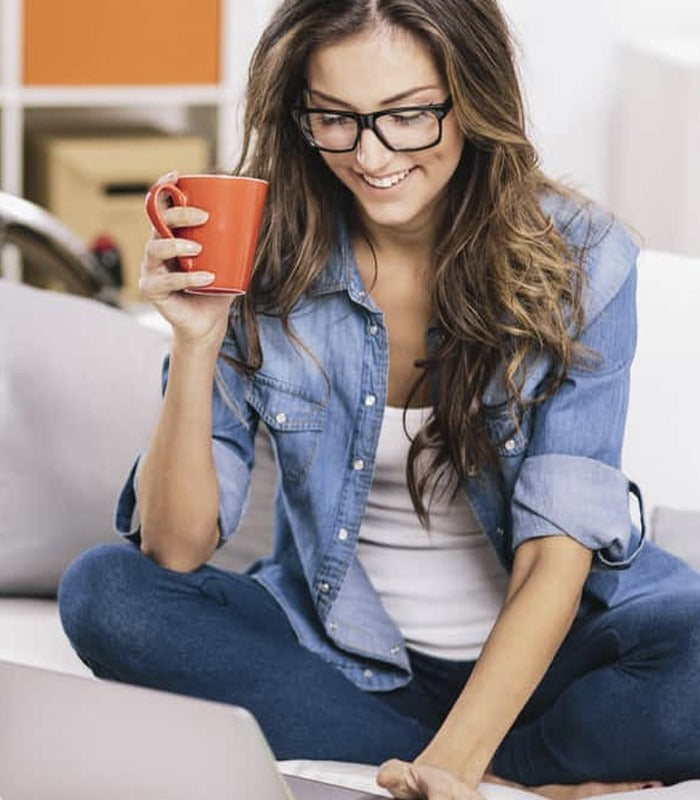Woman working on a laptop at home while holding a cup