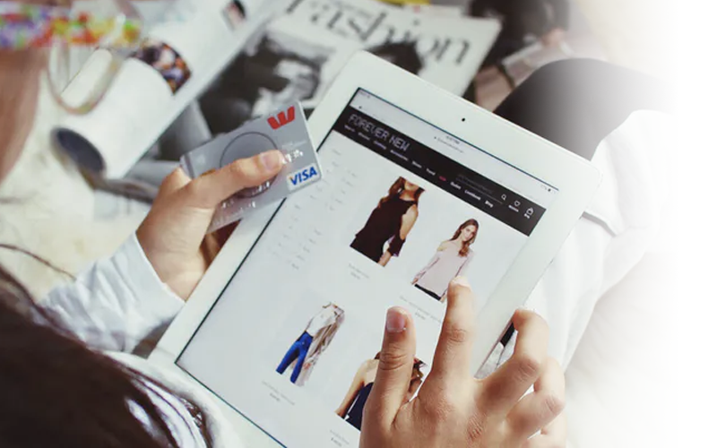 Shopper browsing clothing on a tablet while holding a payment card