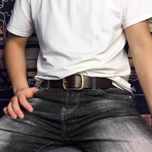 Brown belt with a rounded brass-coloured buckle worn with a white T-shirt and dark jeans